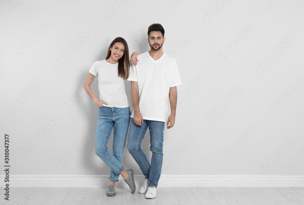 Young couple in stylish jeans near light wall Young couple in stylish jeans near light wall