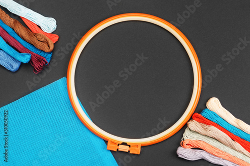 Embroidery hoop with multicolor threads for needlework and sewing on black background. Embroidery accessories concept, mock-up with copy space. Flat layout, top view.