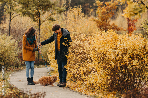 Young couple with a red cat on a background of an autumn park.