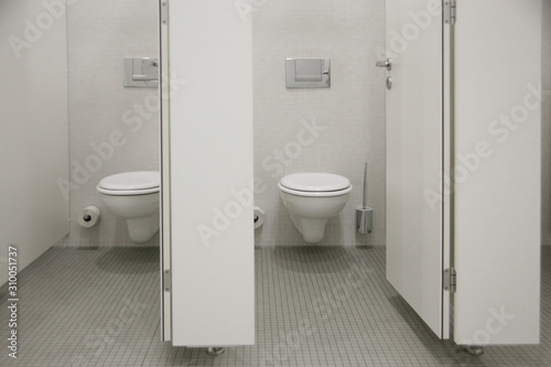 Toilet bowls in public bathroom  restroom or WC maintained in sterile condition for high standards of lavatory hygiene. Interior photo in shades of white of gray. 