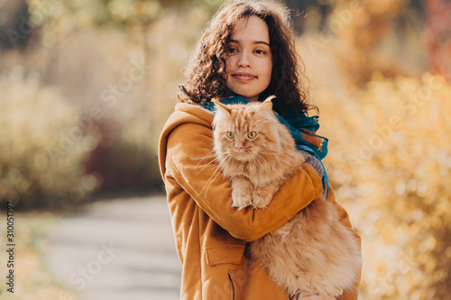 A girl walks with a red cat along the autumn street.