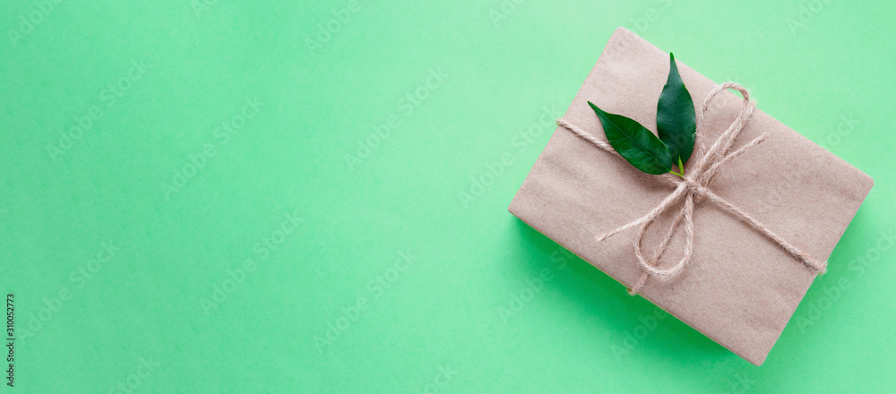 Gift box wrapped in kraft paper tied with twine decorated with two green leaves on neo mint background. Trend color 2020. Banner. DIY. Zero waste holidays concept. Flat lay. Copy space Gift box wrapped in kraft paper tied with twine decorated with two green leaves on neo mint background. Trend color 2020. Banner. DIY. Zero waste holidays concept. Flat lay. Copy space