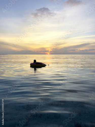 Silhouette eines Mannes einsam auf dem indischen Ozean in einem Rettungsring im Abendrot