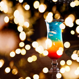 Rainbow cocktail on the bar stand with dark background. Shallow DOF with festive bokeh lights