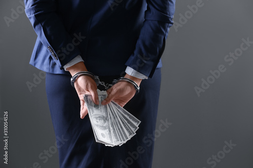 Woman in handcuffs holding bribe money on dark background, closeup