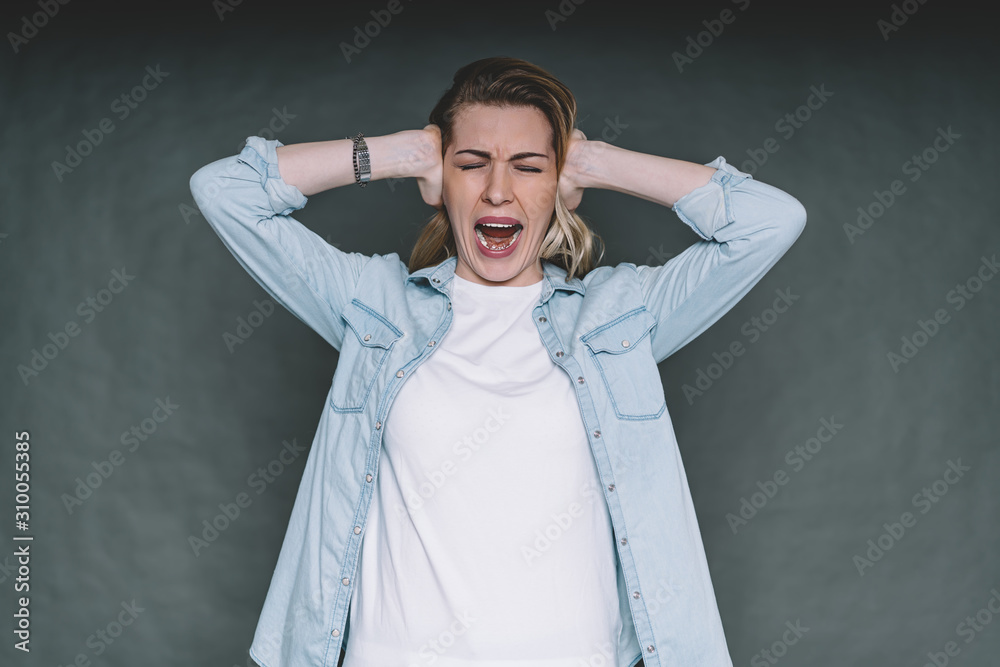 Woman screaming covering ears with hands in studio