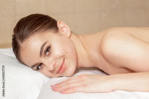 Caucasian young woman lying down on towel smiling during massage in spa.