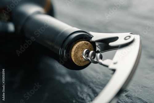 Stainless  wine corkscrew in a cork of wine bottle neck on a black slate background