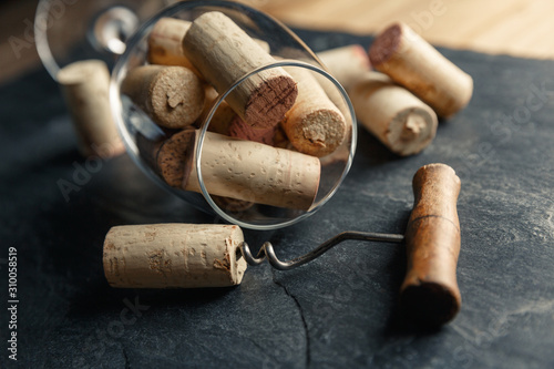 Wine corkscrew and wine glass full of corks on a black slate background