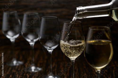 white wine pouring into glasses from bottle, selective focus