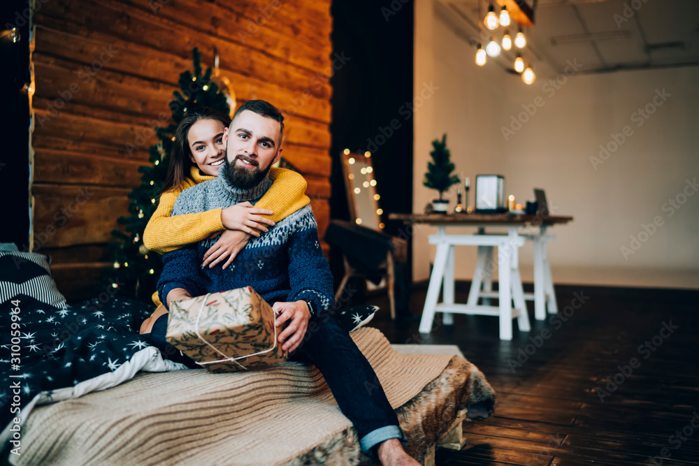 Beautiful cheerful couple sitting on bed with Christmas present