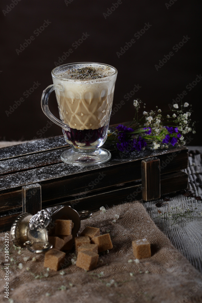 Coffee drink with lavender syrup. A glass tumbler sits on a wooden box with a vintage sugar bowl. The drink is served in layers. Copy space.
