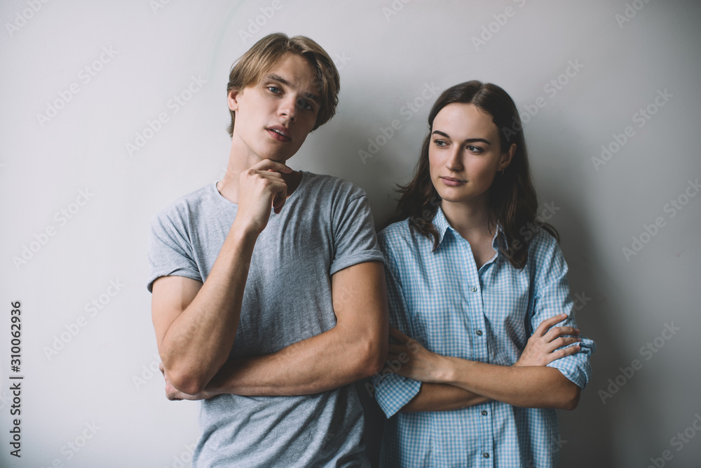 Half length portrait of pensive hipster guy in casual outfit posing at promotional background during free time with female friend, Caucasian couple standing at publicity area and thinking indoors Half length portrait of pensive hipster guy in casual outfit posing at promotional background during free time with female friend, Caucasian couple standing at publicity area and thinking indoors