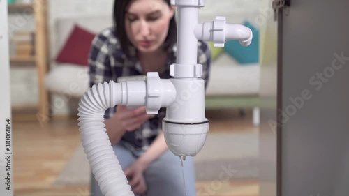 Young woman discovered a leak under the sink and calls the plumber