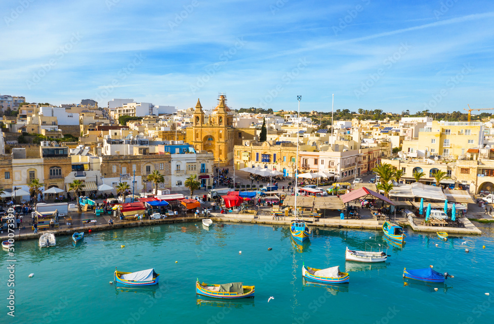 Landscape view of fishing village Marsaxlokk. Traditional maltese boats on the sea, main church, coastline, blue sly. Malta