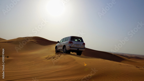 Off-roading: a jeep drives over large red sand dunes in the desert of the United Arab Emirates, the sunset and blue sky in the backgrpound