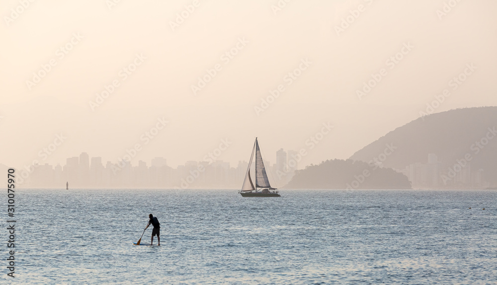 Typical summer afternoon scene in the city of Santos, with sailboats and stand up paddle practitioner