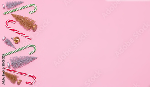 Christmas border design with gold and silver christmas trees, striped sticks lollipops and copy space on a pink background. 