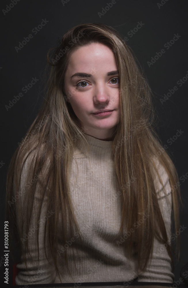Portrait of a beautiful, sweet, young girl on a gray background in a beige sweater