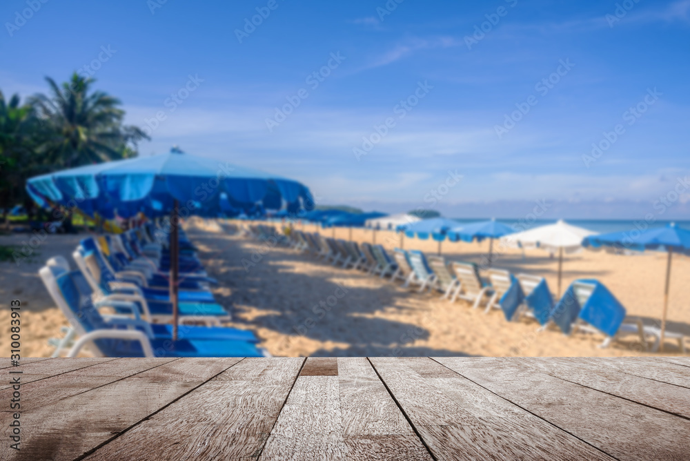 Wooden table top on blurred umbrella and some people relax on the white sand beach and blue sea with blue sky