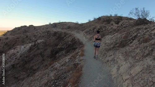 A tattooed woman with black hair enters from out of frame and walks along a desert mountain trail in Bermuda Dunes, California photo