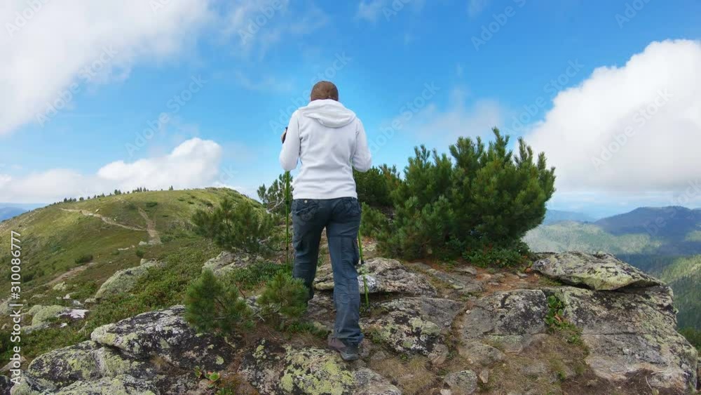 Woman with trekking poles climbs to the top of the mountain and enjoys the view. Slow motion Woman with trekking poles climbs to the top of the mountain and enjoys the view. Slow motion