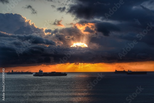 a sunrise from Algeciras, the sun behind the clouds with some bay boats