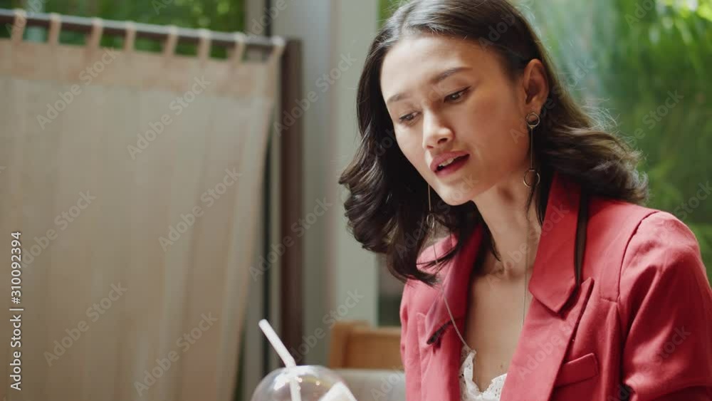 Attractive Asian woman sips ice coffee, enjoys the rich taste then looks at her friend and smiles and laughs Attractive Asian woman sips ice coffee, enjoys the rich taste then looks at her friend and smiles and laughs