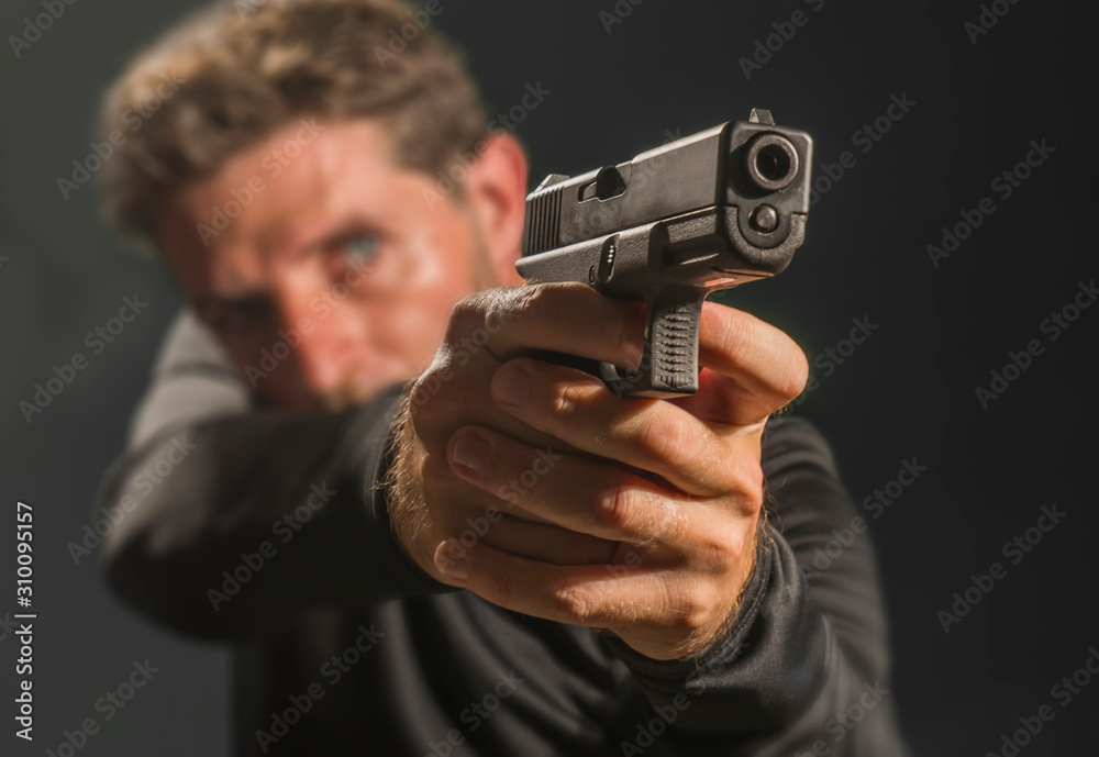 shallow depth of focus action portrait of serious and attractive hitman or special agent man holding gun pointing the weapon isolated on dark background shallow depth of focus action portrait of serious and attractive hitman or special agent man holding gun pointing the weapon isolated on dark background