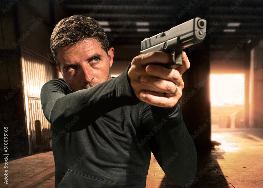 action portrait of serious and attractive hitman or special agent man holding gun pointing the weapon at cinematic edgy background in secret service movie Hollywood style action portrait of serious and attractive hitman or special agent man holding gun pointing the weapon at cinematic edgy background in secret service movie Hollywood style
