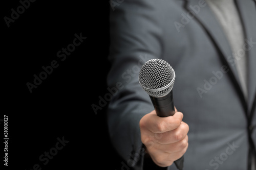 Interviewer or reporter with a microphone in hand, on an insulated black background. Grey jacket