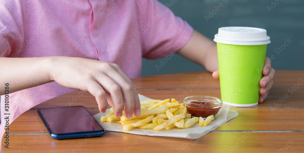 a child sits at a table, drinking a drink from a disposable glass and eating French fries with sauce, close-up