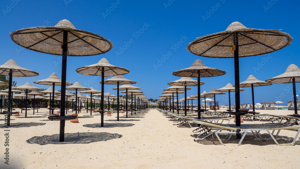 Marsa Matruh, Egypt. Rows of umbrellas made of straw and sunbeds. Sandy beach. Sunrise and early morning time. Relaxing context. Fabulous holidays. Mediterranean Sea. North Africa