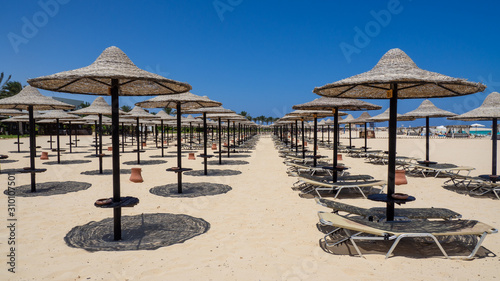 Marsa Matruh, Egypt. Rows of umbrellas made of straw and sunbeds. Sandy beach. Sunrise and early morning time. Relaxing context. Fabulous holidays. Mediterranean Sea. North Africa