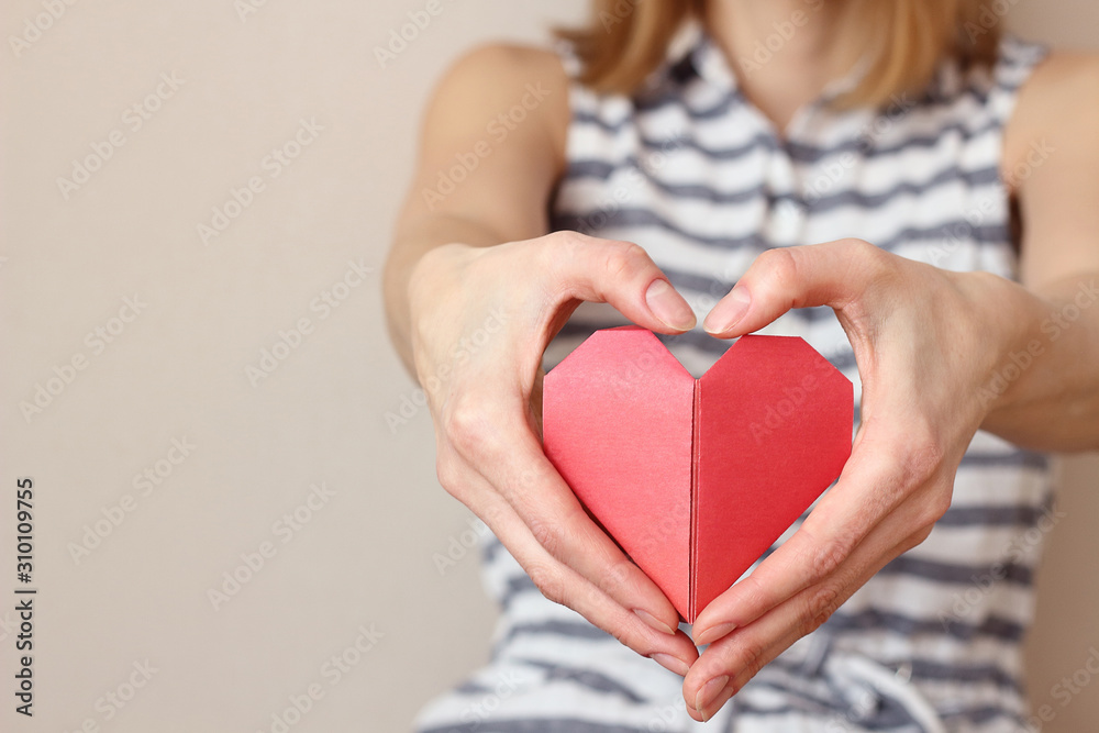 caucasian woman folds her hands in the shape of a heart and holds an origami paper heart, insurance, charity donation concept. Place for text copy space, selective focus caucasian woman folds her hands in the shape of a heart and holds an origami paper heart, insurance, charity donation concept. Place for text copy space, selective focus