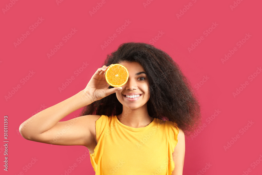 Happy African-American woman with orange fruit piece on color background