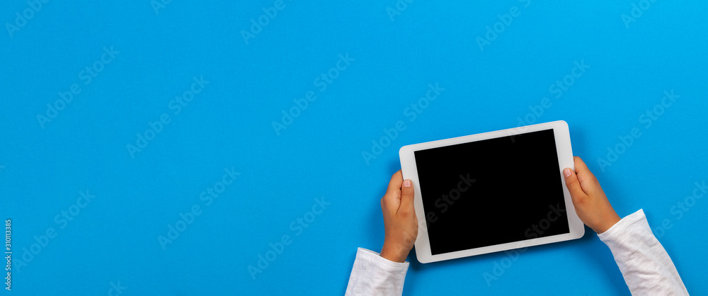 Kid hand holding white tablet computer on light blue background - obrazy, fototapety, plakaty 