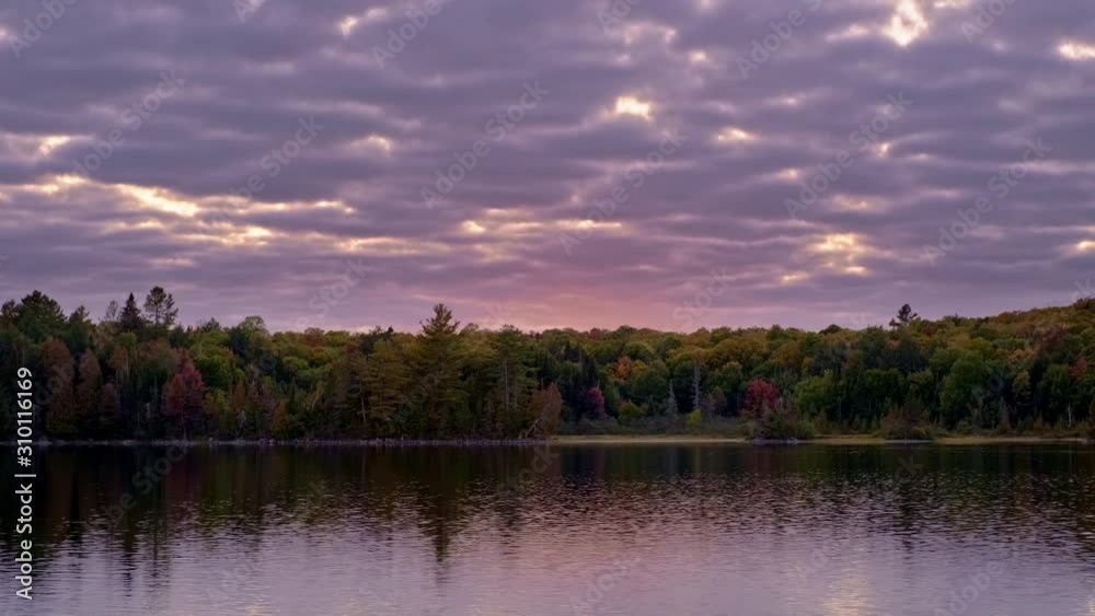 Purple Sunrise Clouds over Calm Lake and Fall Leaf Color, Fixed Wide. Sunlight shines through Gaps in Overcast Sky to Light Shore, Autumn Forest Trees, and Water Reflection. Killarney Ontario Canada Purple Sunrise Clouds over Calm Lake and Fall Leaf Color, Fixed Wide. Sunlight shines through Gaps in Overcast Sky to Light Shore, Autumn Forest Trees, and Water Reflection. Killarney Ontario Canada