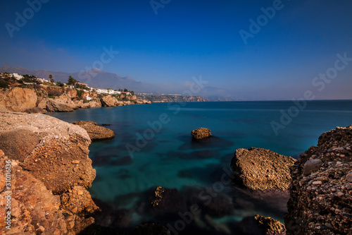 Beach section on the Spanish coast of Costa del Sol in Nerja. Sunny day with blue Mediterranean waters with rocks and city in the background