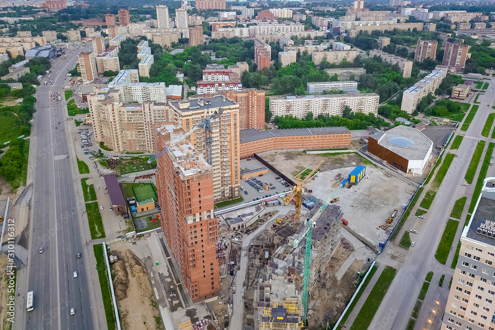 Aerial view of a building construction site at the place of storage of building materials for crushed stone and bricks cement, surrounded by a green lawn with grass at sunset near road in the city
