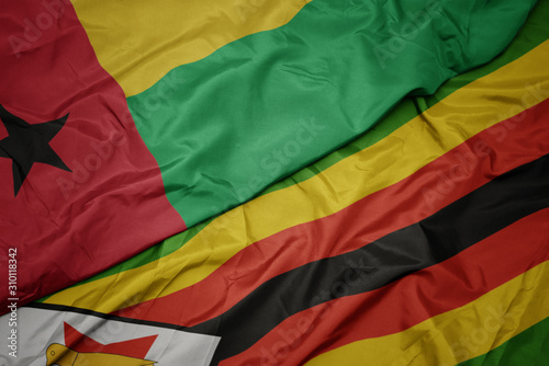 waving colorful flag of zimbabwe and national flag of guinea bissau.