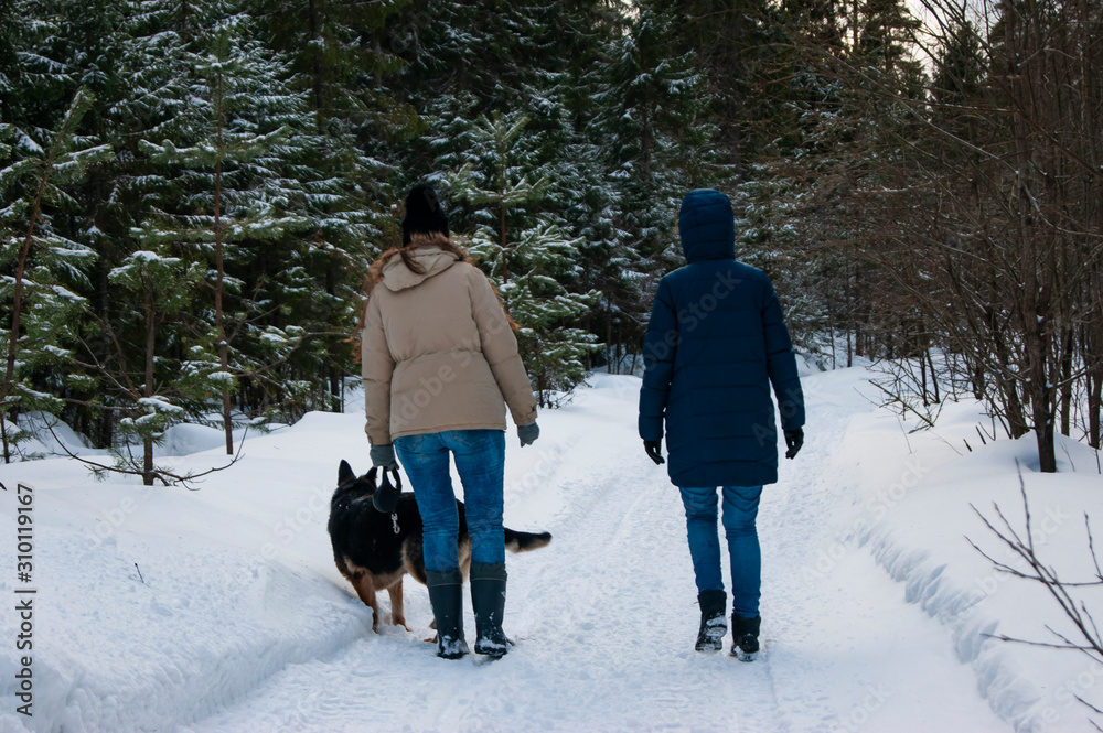 Two girls and a dog are walking in the winter forest