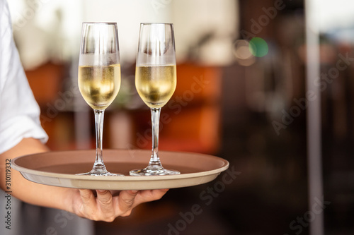 Hand of the waiter brings glasses with champagne on a tray.