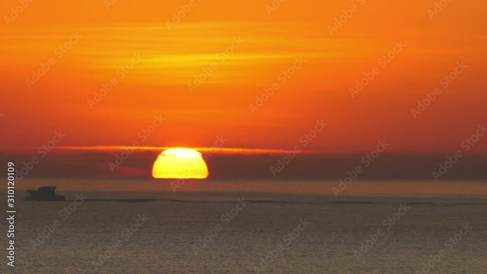 Small motor boat at dawn, big sun rising over ocean, slow motion Small motor boat at dawn, big sun rising over ocean, slow motion