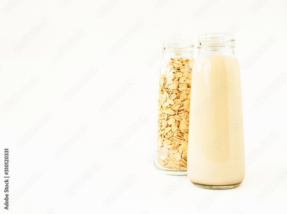 Vegan oat milk and oat flakes in glass bottles on a light background with space for text. Vegan oat milk and oat flakes in glass bottles on a light background with space for text.