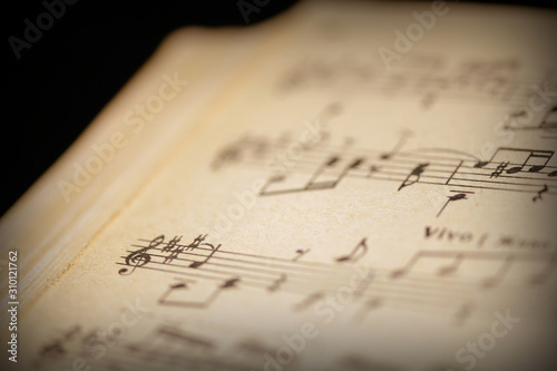 Fragment of a page from an old musical notebook on a dark surface close-up. Music background retro style toned