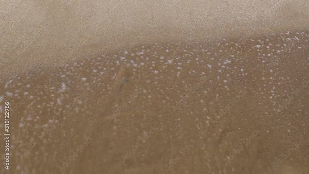 Handwritten inscription 5% on a sandy sea beach is washed by the sea wave with foam on a summer sunny day. Disappearing statistics and percent writing