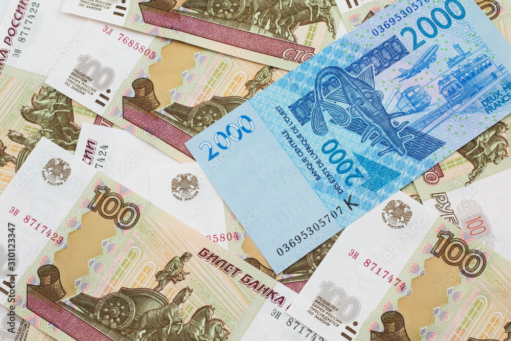 A close up image of a blue, two thousand, West African franc bank note in macro on a background of United States one dollar bills