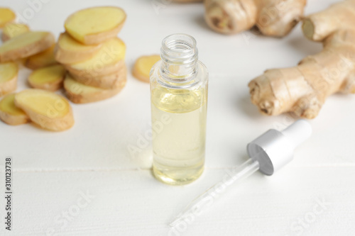 Bottle with ginger essential oil on white table
