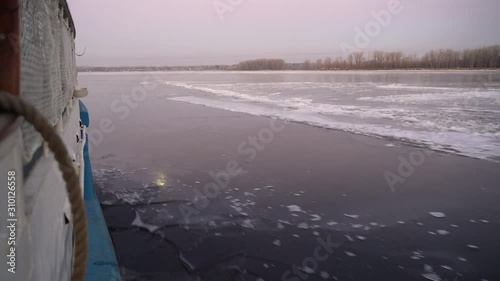 Cargo ferry with the inscription on Board Oksky 35, floats on the ice-bound big river, breaking the thin ice. December morning. photo